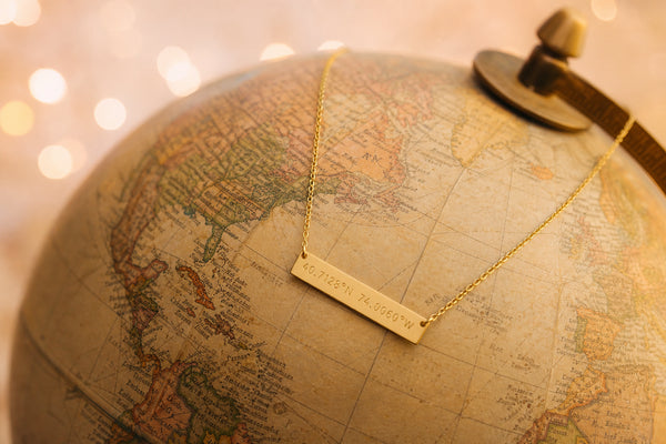 Gold coordinates necklace draped over vintage globe - 50 romantic places for coordinates jewelry