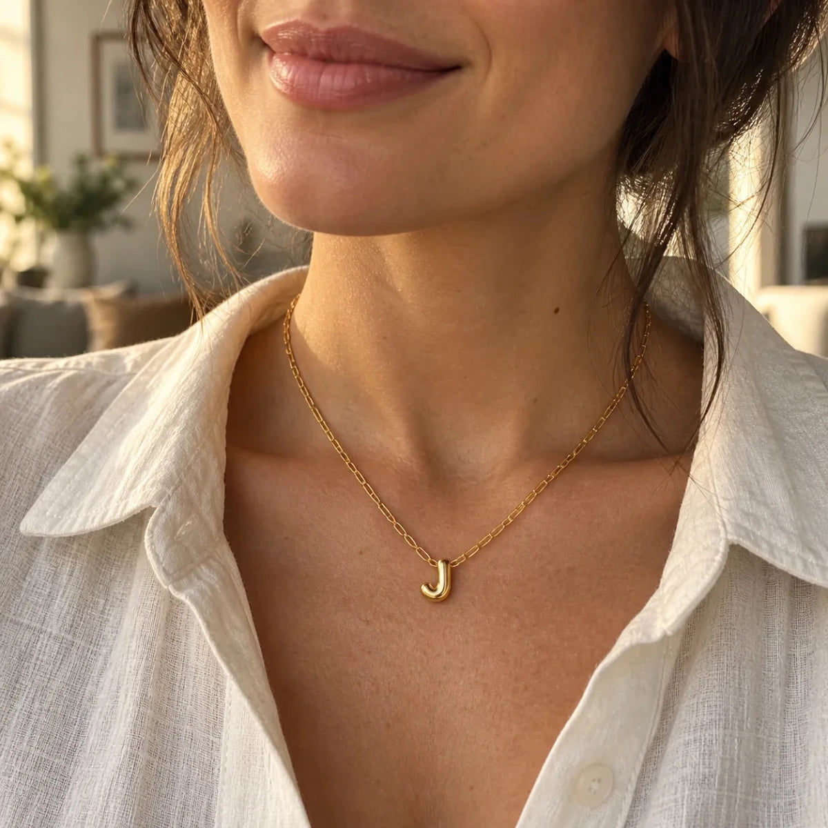Polished gold 3D bubble letter J necklace worn with a white linen shirt.