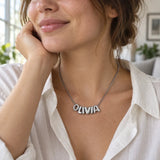 Polished silver 3D bubble necklace spelling OLIVIA, worn with an off-white cotton blouse.