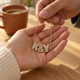 Gold zircon K&Y bubble letter necklace being given by hand at a kitchen table.