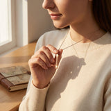 Person holding a necklace with a pendant in a softly lit room.