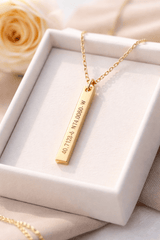 Gold coordinate necklace with a bar pendant in a white jewelry box, surrounded by soft flowers.