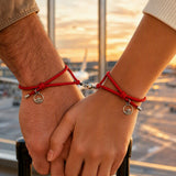 Two people wearing matching red magnetic couple bracelets while holding hands