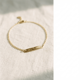 Gold bracelet with engraved coordinates on a light fabric background