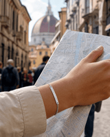 Hand holding a map wearing a silver coordinates chainlink bracelet with a blurred cityscape in the background