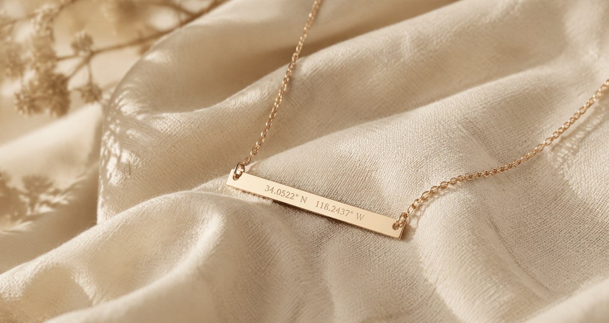 Gold bar necklace engraved with coordinates, resting on cream linen